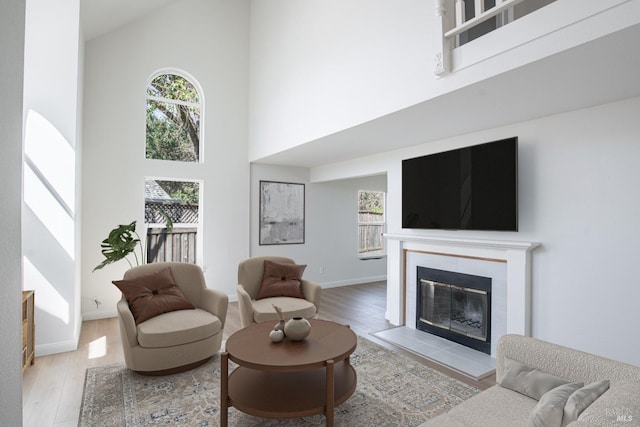 living area featuring a towering ceiling, a healthy amount of sunlight, wood finished floors, and a tiled fireplace