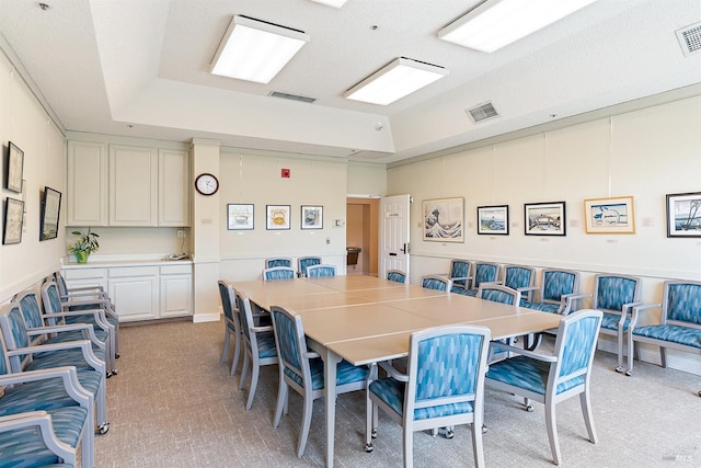 dining space featuring visible vents, a raised ceiling, and light carpet