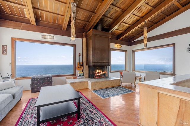 living room featuring light wood finished floors, lofted ceiling with beams, a fireplace, a water view, and wooden ceiling