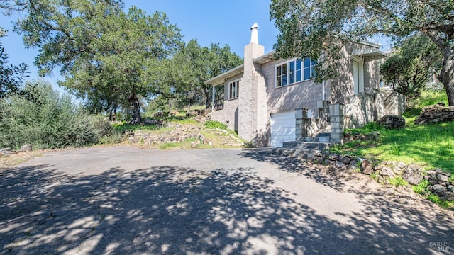 view of home's exterior featuring a chimney, aphalt driveway, and a garage