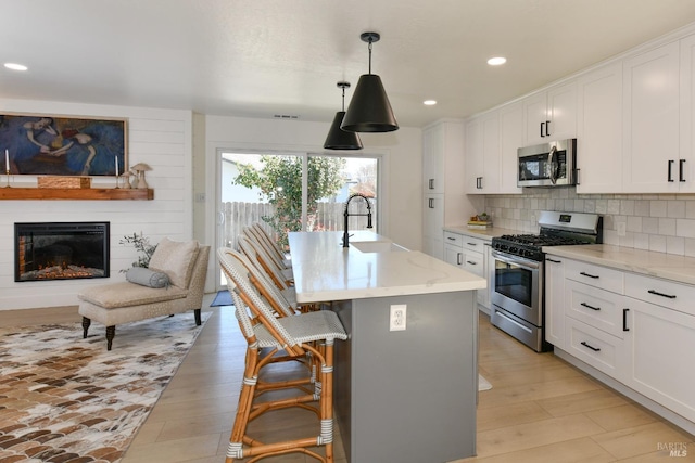 kitchen featuring tasteful backsplash, a sink, appliances with stainless steel finishes, white cabinets, and a kitchen island with sink