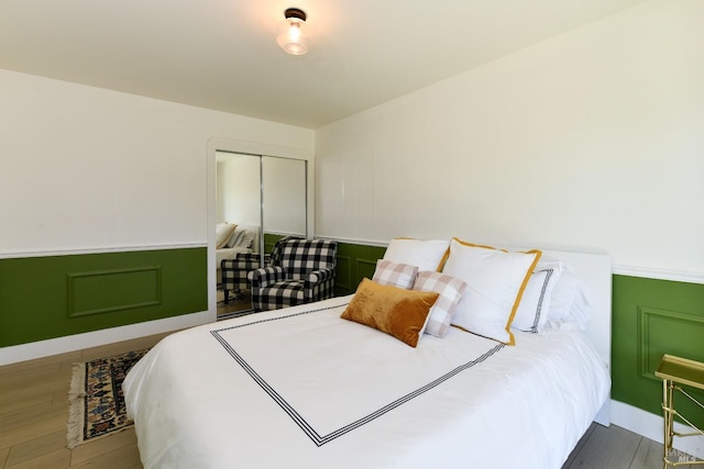 bedroom with a decorative wall, wood finished floors, a closet, and wainscoting