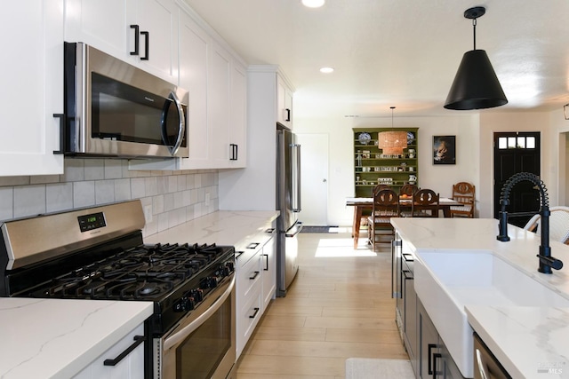 kitchen with decorative light fixtures, decorative backsplash, appliances with stainless steel finishes, white cabinets, and a sink