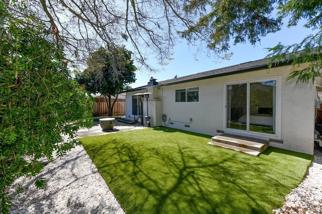 back of house featuring fence, entry steps, stucco siding, a yard, and a patio area