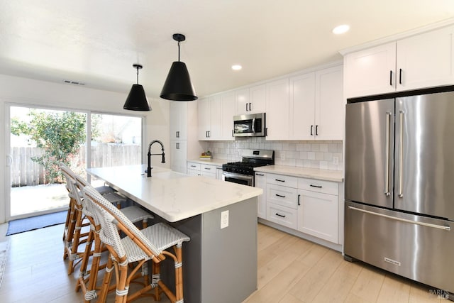 kitchen featuring visible vents, an island with sink, decorative backsplash, appliances with stainless steel finishes, and white cabinets