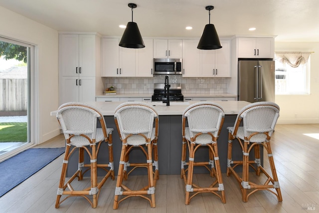 kitchen with tasteful backsplash, appliances with stainless steel finishes, a center island with sink, and light countertops