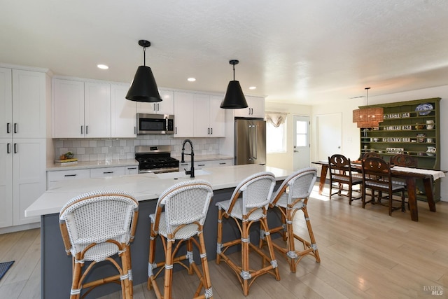 kitchen featuring a sink, backsplash, white cabinetry, stainless steel appliances, and light wood-style floors