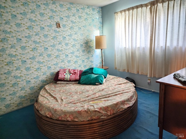 bedroom featuring wallpapered walls, baseboards, and dark colored carpet