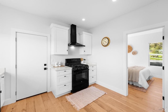 kitchen with black gas range oven, light countertops, wall chimney exhaust hood, and light wood-style floors