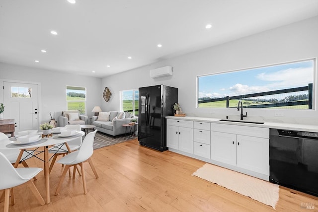 kitchen with a sink, black appliances, light countertops, a wall mounted air conditioner, and light wood-type flooring