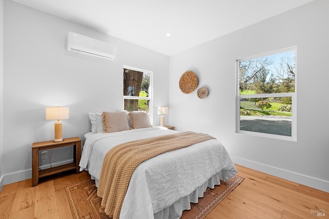 bedroom with multiple windows, an AC wall unit, and wood finished floors