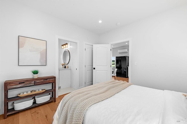 bedroom with connected bathroom, light wood-type flooring, a wall unit AC, recessed lighting, and freestanding refrigerator