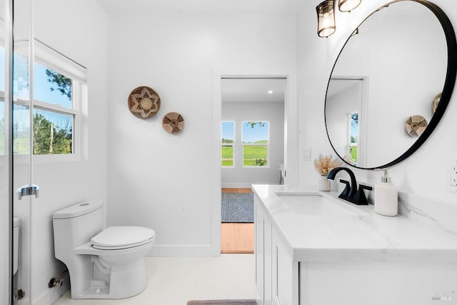 bathroom with toilet, plenty of natural light, vanity, and baseboards