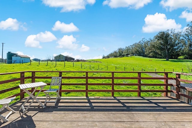 wooden deck featuring a rural view, a lawn, and fence