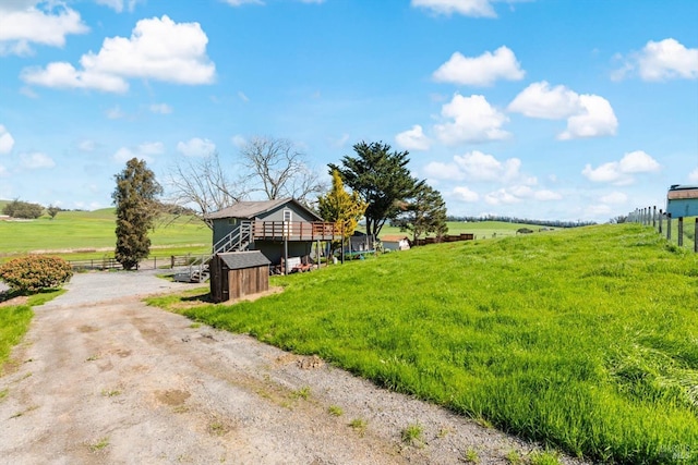 view of yard with a deck, a rural view, fence, and dirt driveway