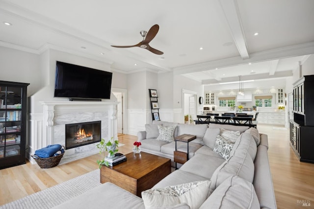 living room featuring light wood finished floors, beamed ceiling, wainscoting, a fireplace, and a decorative wall