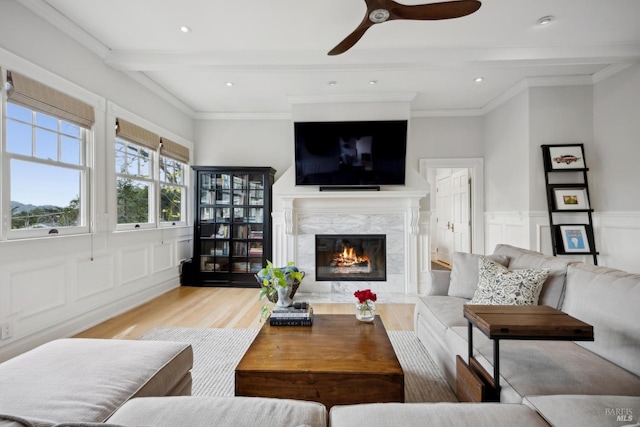 living area featuring wood finished floors, a wainscoted wall, beam ceiling, a high end fireplace, and a decorative wall