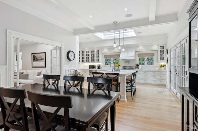 dining area with beam ceiling, a skylight, recessed lighting, and light wood-style floors