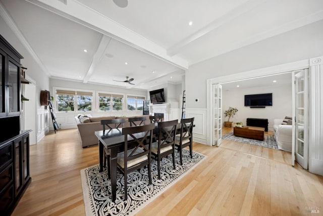 dining room with light wood-type flooring, beamed ceiling, a wainscoted wall, a fireplace, and a decorative wall