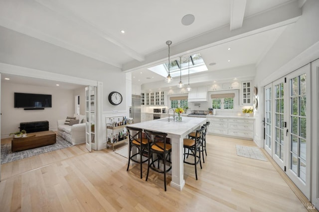 dining area featuring beam ceiling, recessed lighting, light wood-style flooring, french doors, and a skylight