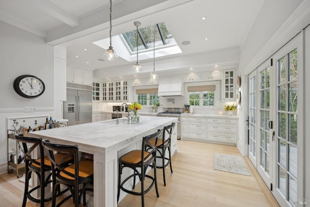 kitchen with high quality appliances, a sink, backsplash, white cabinetry, and a skylight