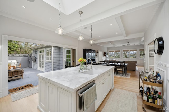 kitchen featuring light wood finished floors, beam ceiling, a sink, white cabinets, and open floor plan