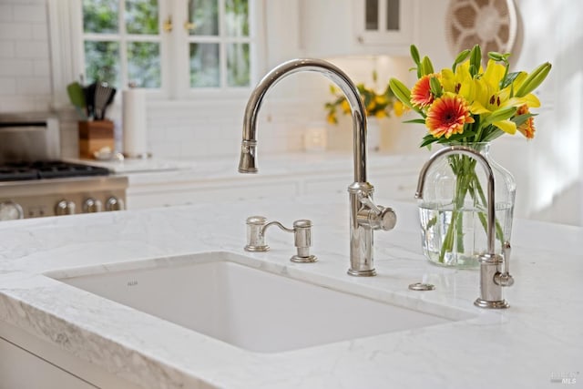 interior details featuring glass insert cabinets, white cabinets, light stone countertops, and a sink