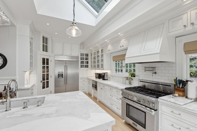 kitchen featuring glass insert cabinets, built in appliances, custom exhaust hood, and white cabinets