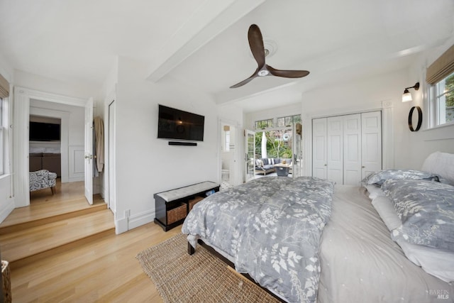 bedroom with beam ceiling, multiple windows, baseboards, and light wood finished floors