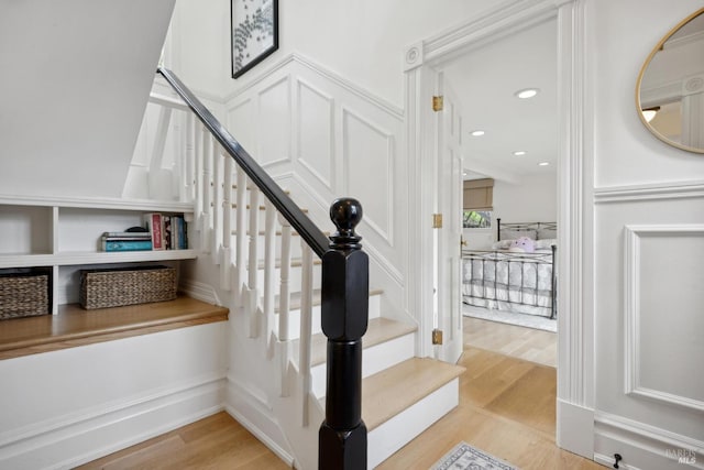 stairway with recessed lighting, wood finished floors, and a decorative wall