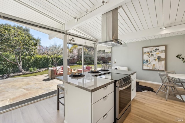 kitchen with light wood-type flooring, beam ceiling, island exhaust hood, stainless steel electric stove, and rail lighting