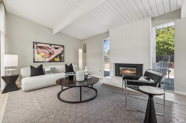 living area featuring visible vents, baseboards, a tiled fireplace, lofted ceiling with beams, and wood finished floors