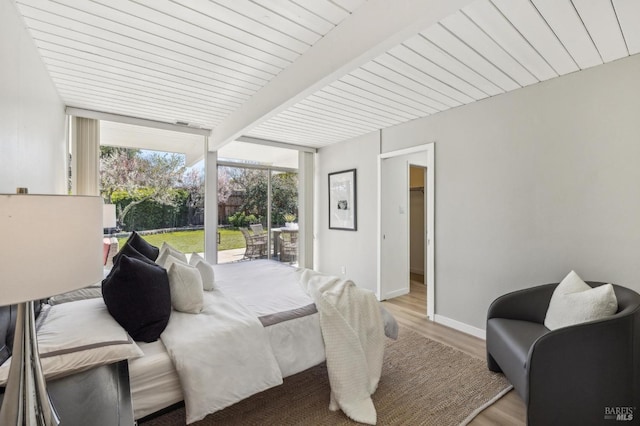 bedroom with beam ceiling, light wood-style flooring, baseboards, and expansive windows