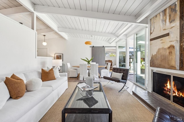 living room featuring lofted ceiling with beams, wood finished floors, a barn door, a lit fireplace, and wooden ceiling