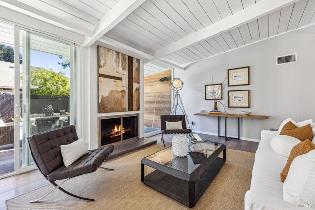 living area featuring visible vents, beamed ceiling, wood finished floors, a fireplace, and baseboards