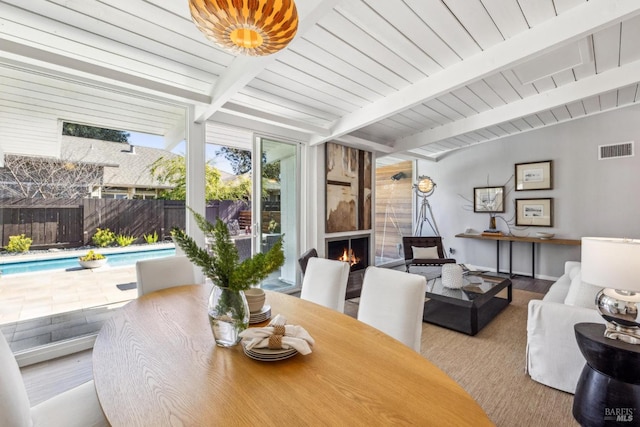 dining space featuring visible vents, wood finished floors, a fireplace, a wall of windows, and vaulted ceiling with beams