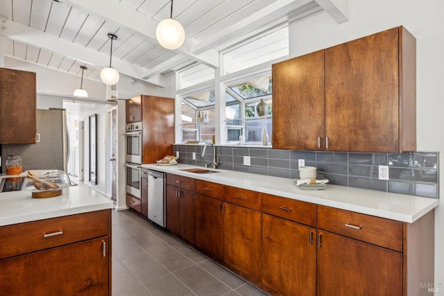 kitchen featuring a sink, light countertops, appliances with stainless steel finishes, dark tile patterned floors, and backsplash