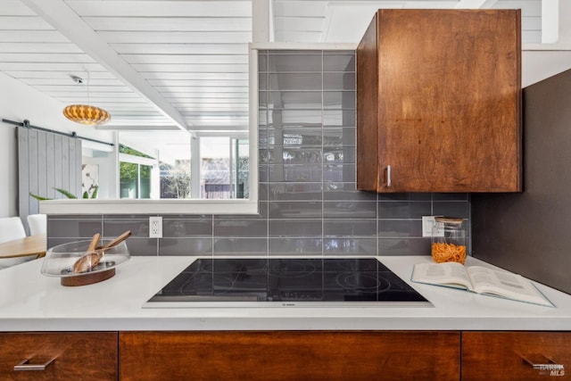 kitchen with a barn door, brown cabinetry, light countertops, decorative backsplash, and black electric stovetop