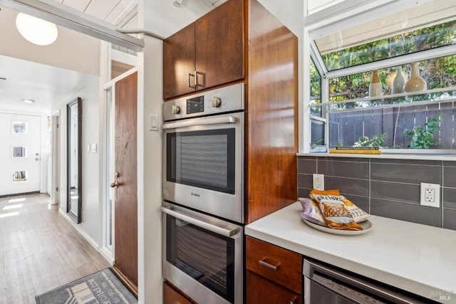 kitchen featuring light wood finished floors, tasteful backsplash, appliances with stainless steel finishes, and light countertops