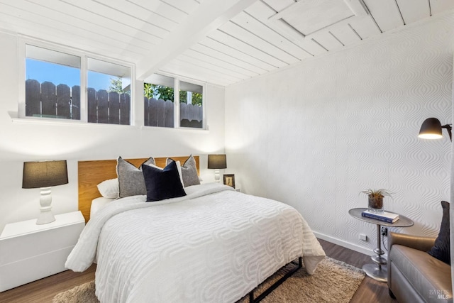 bedroom with wood finished floors, baseboards, wallpapered walls, lofted ceiling with beams, and wooden ceiling