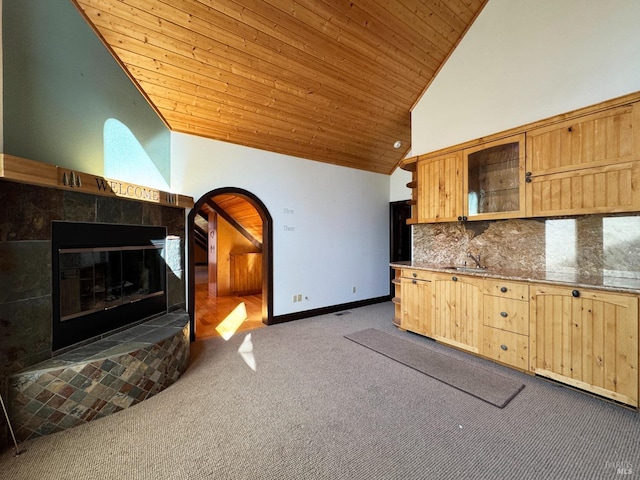 kitchen featuring light brown cabinets, carpet, wooden ceiling, arched walkways, and a sink