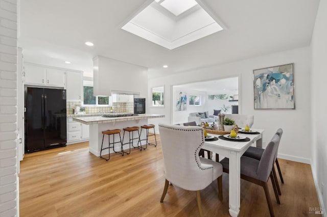 dining area with a skylight, baseboards, light wood-style flooring, and recessed lighting