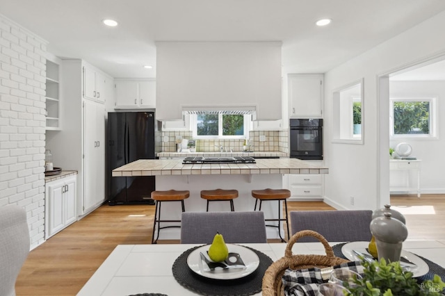 kitchen featuring tile countertops, black appliances, light wood-style flooring, and white cabinetry