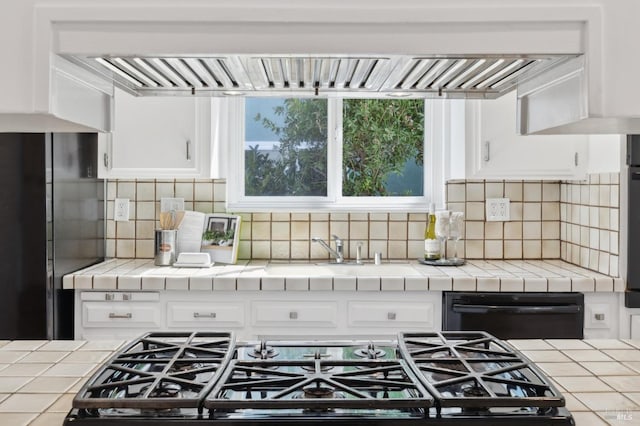 kitchen with tasteful backsplash, gas stovetop, tile countertops, white cabinets, and dishwasher