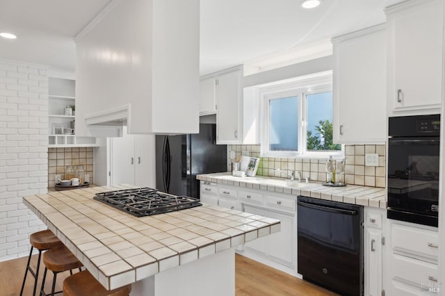 kitchen featuring black appliances, light wood-style flooring, white cabinetry, a breakfast bar area, and tile counters