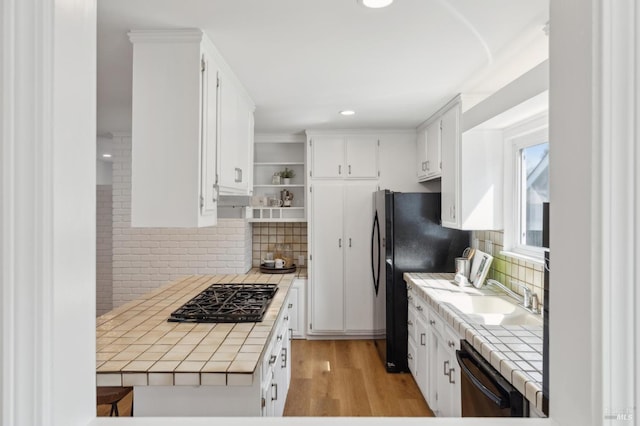 kitchen featuring black appliances, a sink, white cabinetry, tile countertops, and light wood-style floors