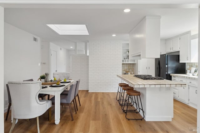 kitchen with a breakfast bar, freestanding refrigerator, white cabinets, light wood finished floors, and tile counters