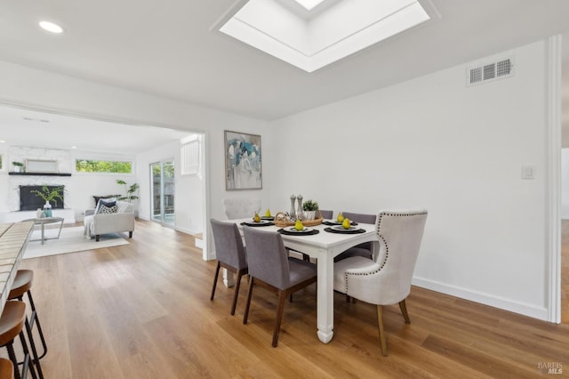 dining area featuring visible vents, a large fireplace, baseboards, light wood-style flooring, and a skylight