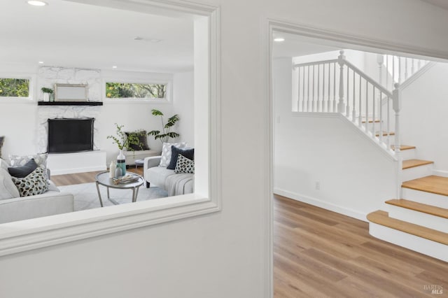 living area with stairs, a stone fireplace, recessed lighting, and wood finished floors