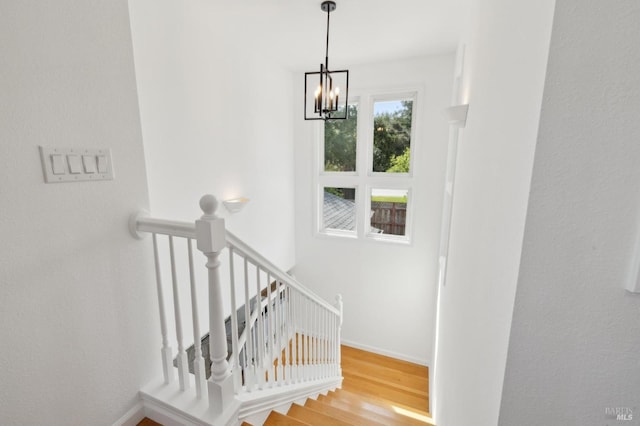 stairs with an inviting chandelier, baseboards, and wood finished floors